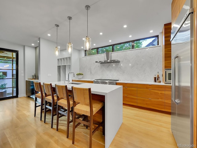 kitchen with wall chimney range hood, tasteful backsplash, a kitchen breakfast bar, a center island with sink, and appliances with stainless steel finishes