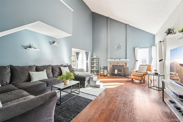 living area with wood-type flooring, high vaulted ceiling, a textured ceiling, and a tile fireplace