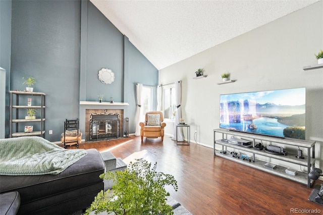 living area with baseboards, a tiled fireplace, high vaulted ceiling, and wood finished floors