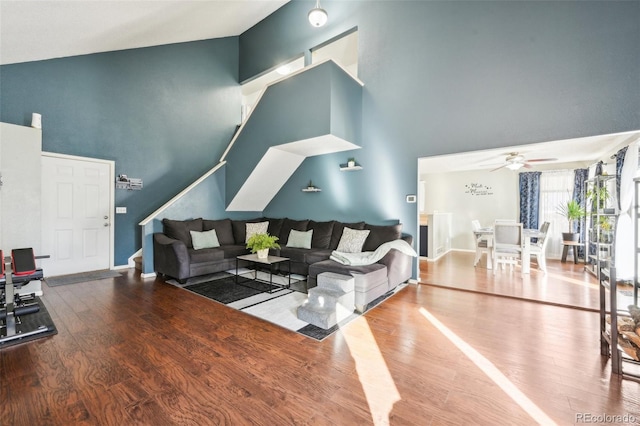 living room with a towering ceiling, ceiling fan, baseboards, and wood finished floors