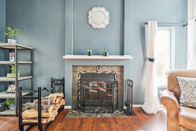 living room with a tile fireplace, baseboards, and wood finished floors