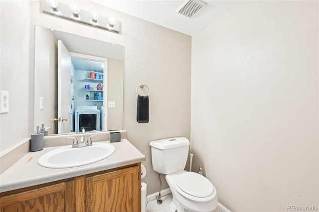 half bathroom with toilet, washer / dryer, vanity, and visible vents