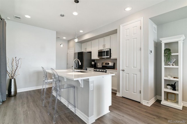 kitchen with appliances with stainless steel finishes, dark wood-type flooring, a kitchen island with sink, white cabinetry, and a kitchen bar