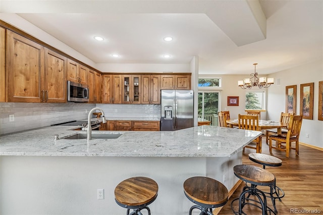 131 Creek Ln, Silverthorne, CO 80498 - kitchen featuring appliances with stainless steel finishes, a peninsula, brown cabinets, light stone countertops, and a kitchen bar