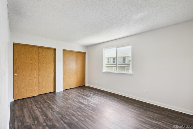 unfurnished bedroom featuring a textured ceiling, multiple closets, and dark hardwood / wood-style floors