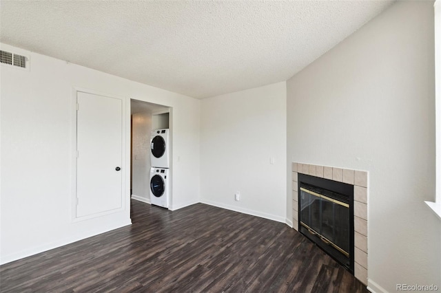 unfurnished living room with dark wood-type flooring, a tile fireplace, stacked washer / dryer, and a textured ceiling