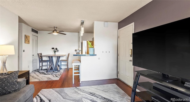 living area featuring a textured ceiling, dark wood-type flooring, visible vents, and a ceiling fan