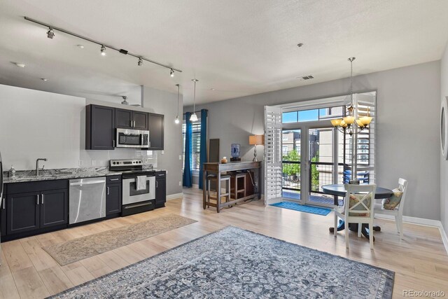 kitchen featuring appliances with stainless steel finishes, light wood-style flooring, light stone countertops, a chandelier, and baseboards