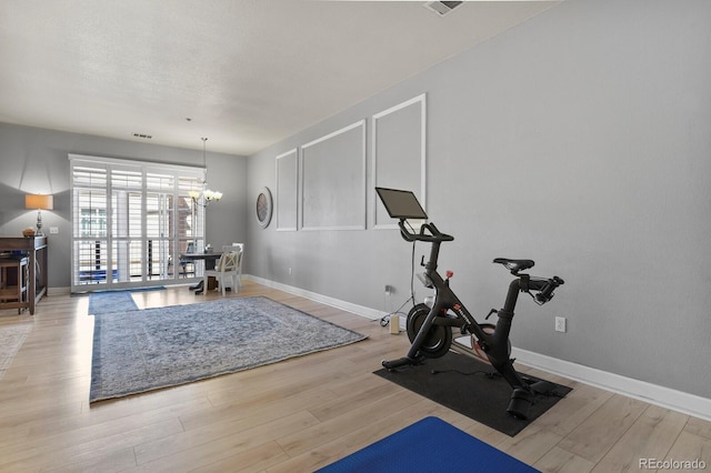 exercise area featuring wood finished floors, a chandelier, and baseboards