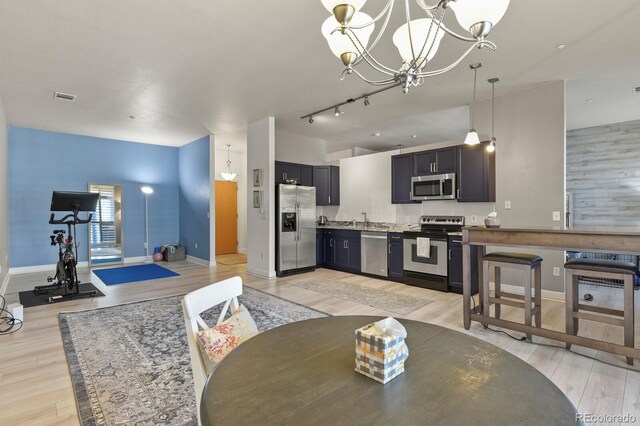 dining space with light wood finished floors, a chandelier, baseboards, and rail lighting