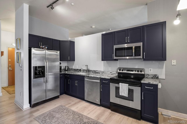 kitchen with stainless steel appliances, light stone counters, light wood-style flooring, baseboards, and a sink