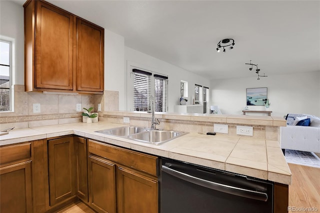 kitchen featuring dishwasher, sink, tasteful backsplash, kitchen peninsula, and light wood-type flooring