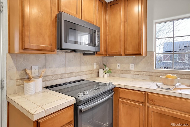 kitchen with tile countertops, backsplash, and appliances with stainless steel finishes