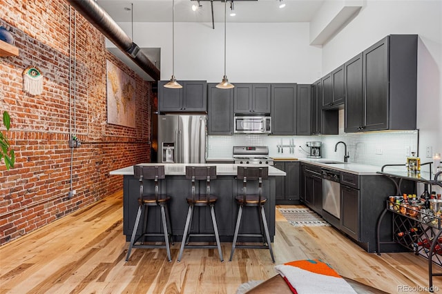 kitchen featuring appliances with stainless steel finishes, a towering ceiling, decorative light fixtures, brick wall, and light hardwood / wood-style floors