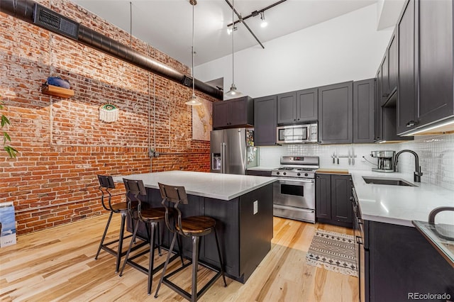 kitchen featuring appliances with stainless steel finishes, a breakfast bar, light wood-type flooring, pendant lighting, and sink