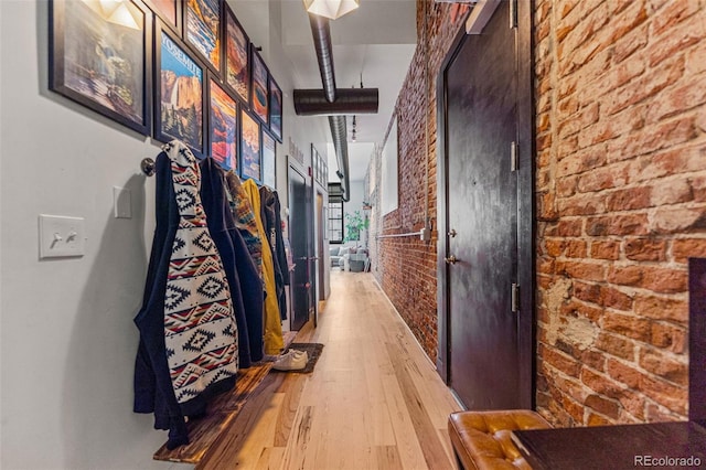 hallway with light hardwood / wood-style floors and brick wall