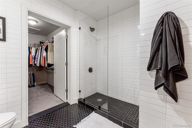 bathroom featuring toilet, tile walls, a shower with shower door, and tile patterned flooring