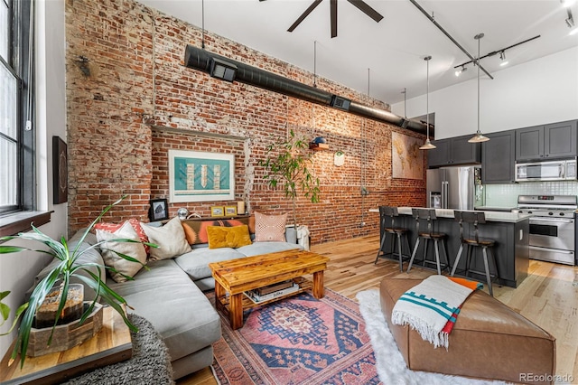 living room featuring light hardwood / wood-style flooring, brick wall, a high ceiling, and ceiling fan