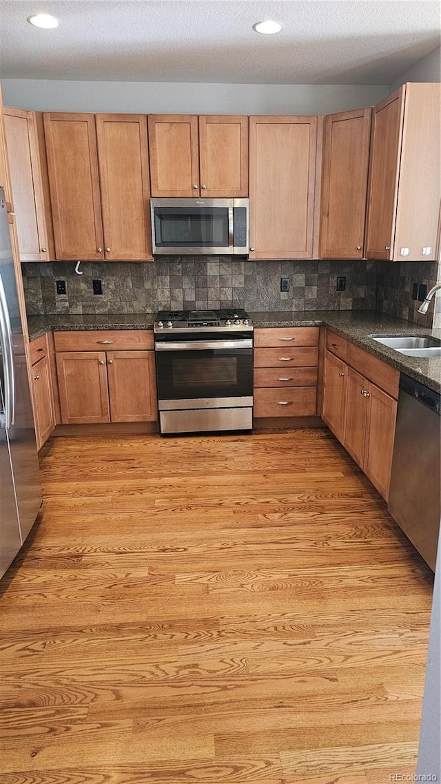 kitchen with stainless steel appliances, sink, dark stone countertops, and light wood-type flooring