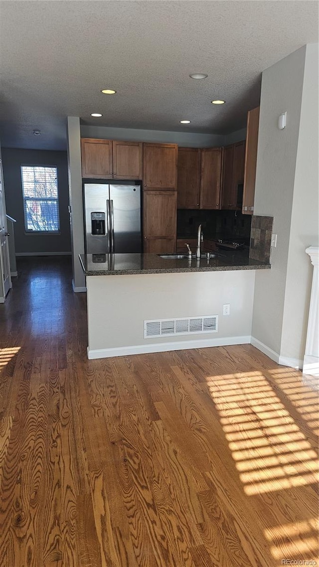 kitchen featuring sink, dark stone countertops, stainless steel fridge, backsplash, and kitchen peninsula