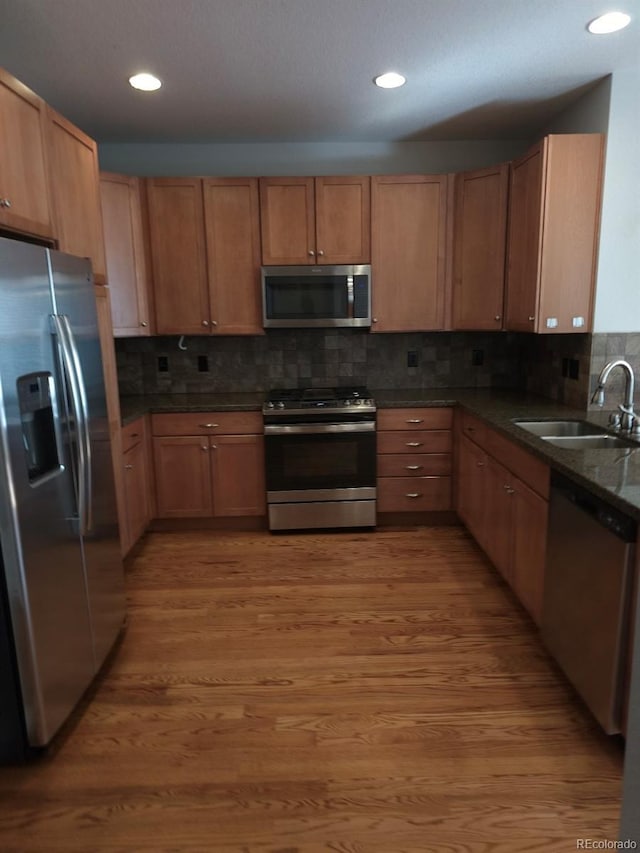 kitchen with sink, wood-type flooring, dark stone countertops, appliances with stainless steel finishes, and backsplash