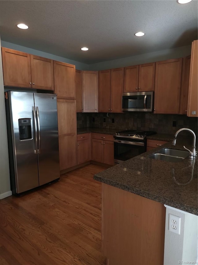 kitchen featuring appliances with stainless steel finishes, sink, dark stone countertops, kitchen peninsula, and dark wood-type flooring