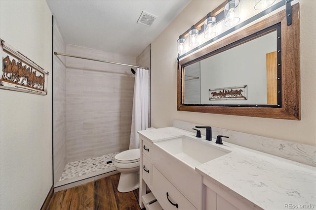 full bath with toilet, tiled shower, wood finished floors, and visible vents