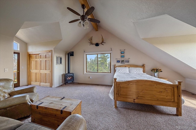 carpeted bedroom featuring lofted ceiling with beams, a textured ceiling, a ceiling fan, baseboards, and a wood stove