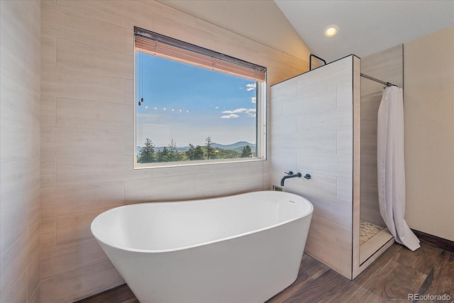 bathroom featuring recessed lighting, wood finished floors, vaulted ceiling, a soaking tub, and a tile shower