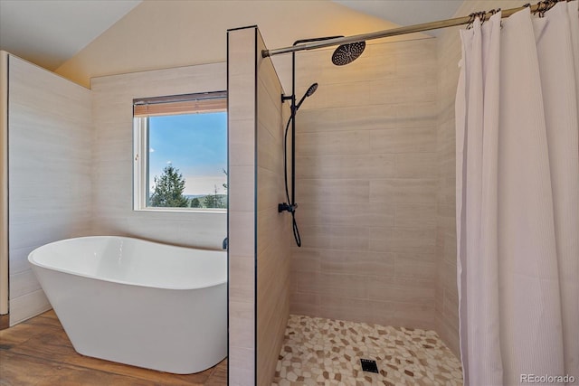 full bath featuring a freestanding tub, tiled shower, vaulted ceiling, and wood finished floors