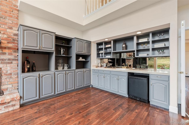 kitchen with dark wood-type flooring, black fridge, sink, gray cabinets, and a towering ceiling