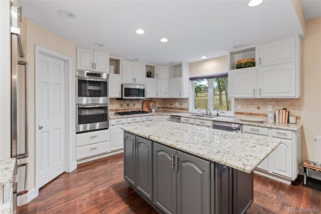 kitchen featuring dark hardwood / wood-style floors, light stone countertops, appliances with stainless steel finishes, a kitchen island, and white cabinetry