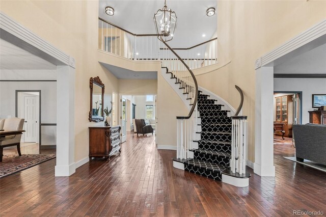 entrance foyer with a notable chandelier, crown molding, dark wood-type flooring, and a high ceiling