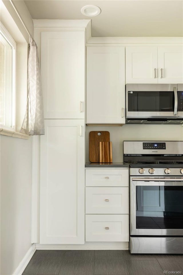 654 S Shoshone St, Denver, CO 80223 - kitchen featuring stainless steel appliances, white cabinets, baseboards, and dark countertops