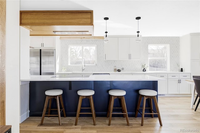 kitchen with stainless steel refrigerator, light wood finished floors, a kitchen bar, and white cabinetry