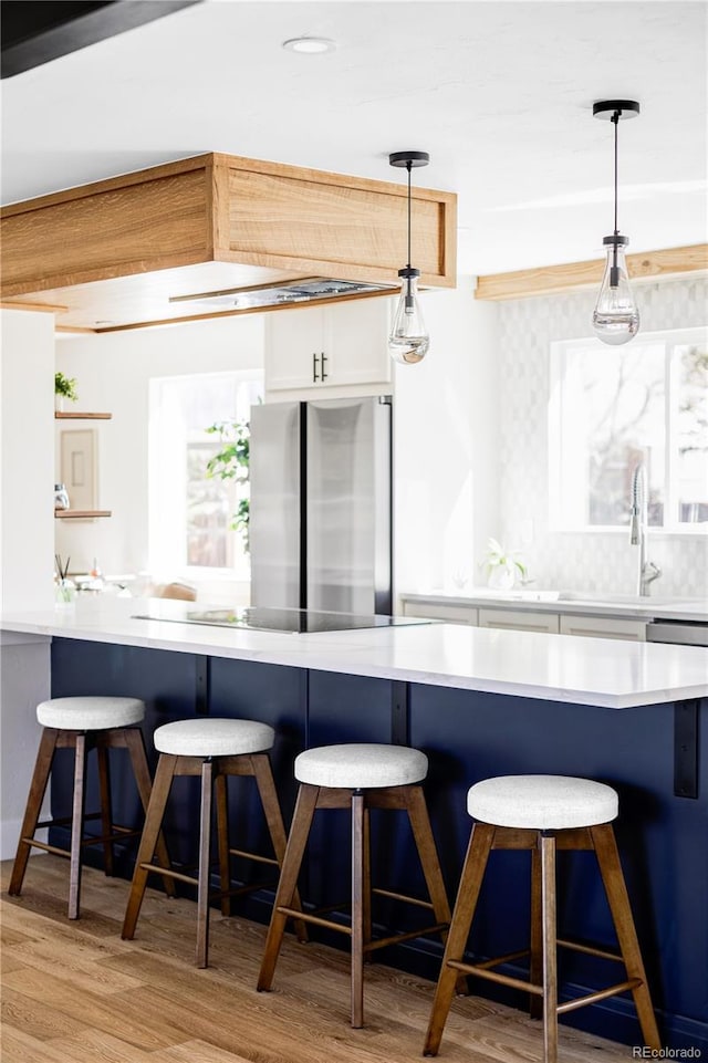 kitchen with freestanding refrigerator, light wood-style floors, a sink, white cabinetry, and a breakfast bar area
