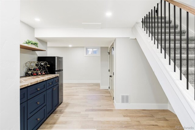 kitchen with blue cabinetry, freestanding refrigerator, light wood finished floors, open shelves, and light countertops
