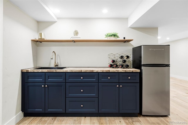 kitchen featuring freestanding refrigerator, open shelves, blue cabinetry, a sink, and light wood finished floors