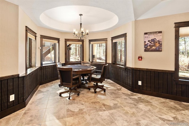 dining space featuring an inviting chandelier, a raised ceiling, a healthy amount of sunlight, and a wainscoted wall