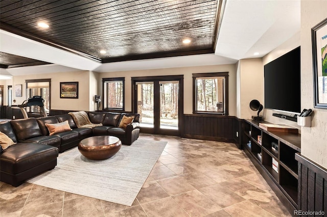 living area featuring french doors, a raised ceiling, a wainscoted wall, and wood walls