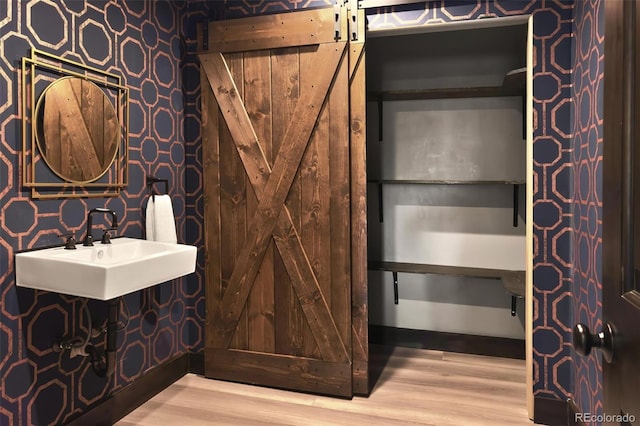 bathroom featuring a sink, wood finished floors, and wallpapered walls