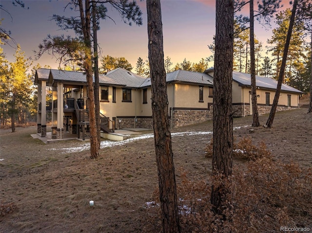 rear view of house with stone siding, stucco siding, and a patio