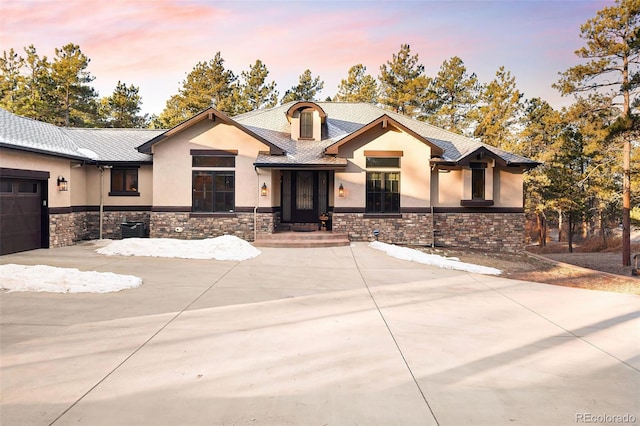 view of front of house featuring concrete driveway, a garage, stone siding, and stucco siding