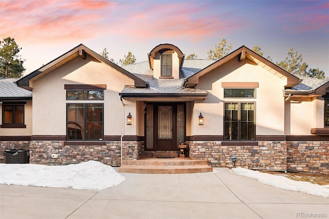 view of front of house with stucco siding, stone siding, and roof with shingles