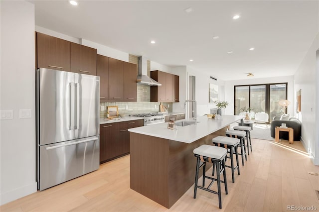 kitchen with appliances with stainless steel finishes, sink, a breakfast bar area, a kitchen island with sink, and wall chimney range hood