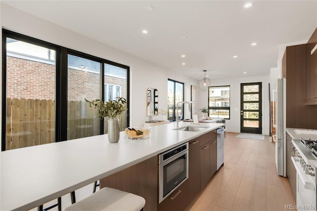 kitchen featuring sink, a breakfast bar area, appliances with stainless steel finishes, pendant lighting, and light hardwood / wood-style floors