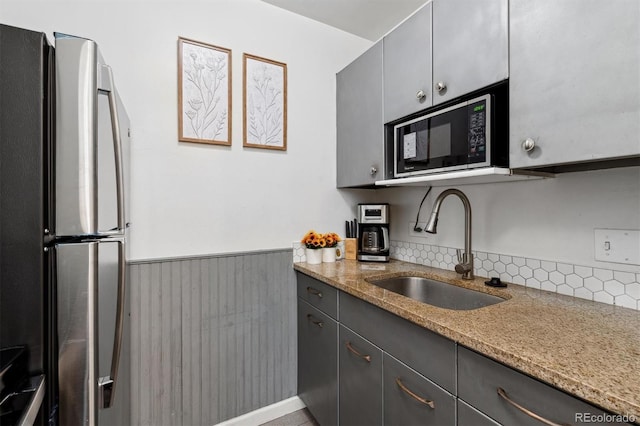 kitchen with sink, stone countertops, and stainless steel refrigerator