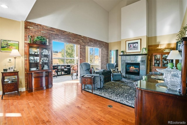 living room featuring hardwood / wood-style floors, a tile fireplace, high vaulted ceiling, and brick wall