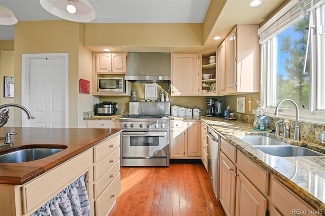 kitchen featuring appliances with stainless steel finishes, sink, light brown cabinetry, and wall chimney exhaust hood