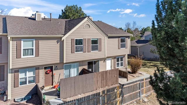multi unit property with a chimney, a shingled roof, and fence